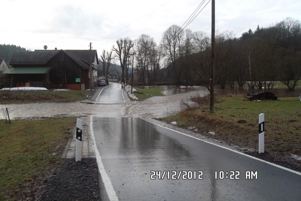 Straße mit wasserführender Senke und nicht überflutetem Haus im Hintergrund