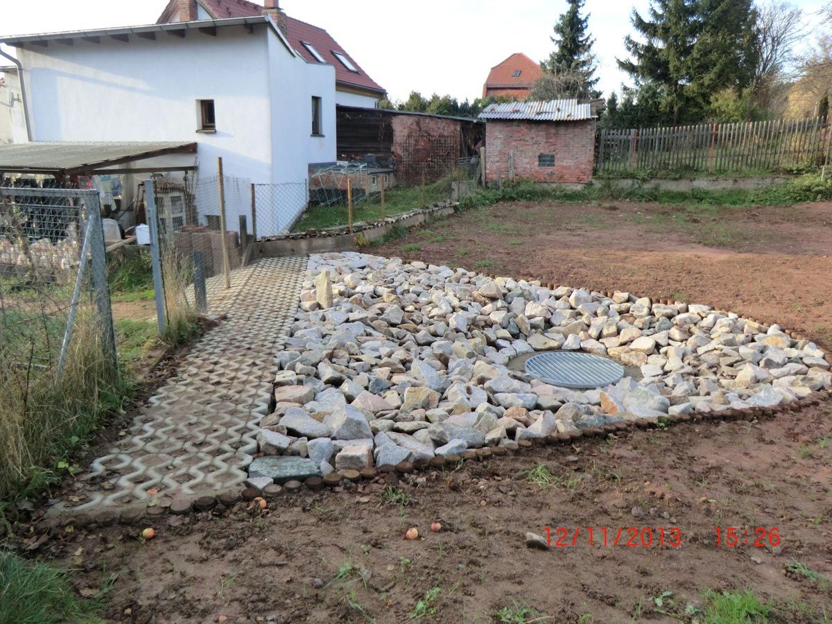 Einlaufschacht mit losen Steinen am Rand auf einem unbewirtschafteten Grundstück in Ortslage